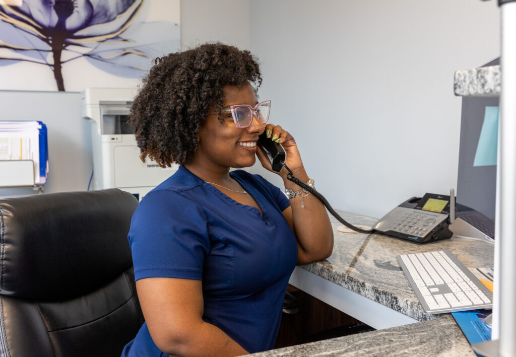 A smiling receptionist at IntraVenous Solutions is taking a phone call about IV therapy near Brentwood, TN.