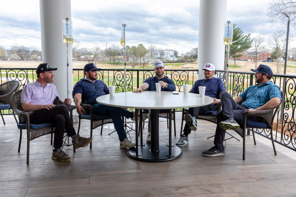 A group of 5 men sit at a table outside on a patio at a golf course receiving anti-aging treatments in Franklin, TN with mobile IV therapy.