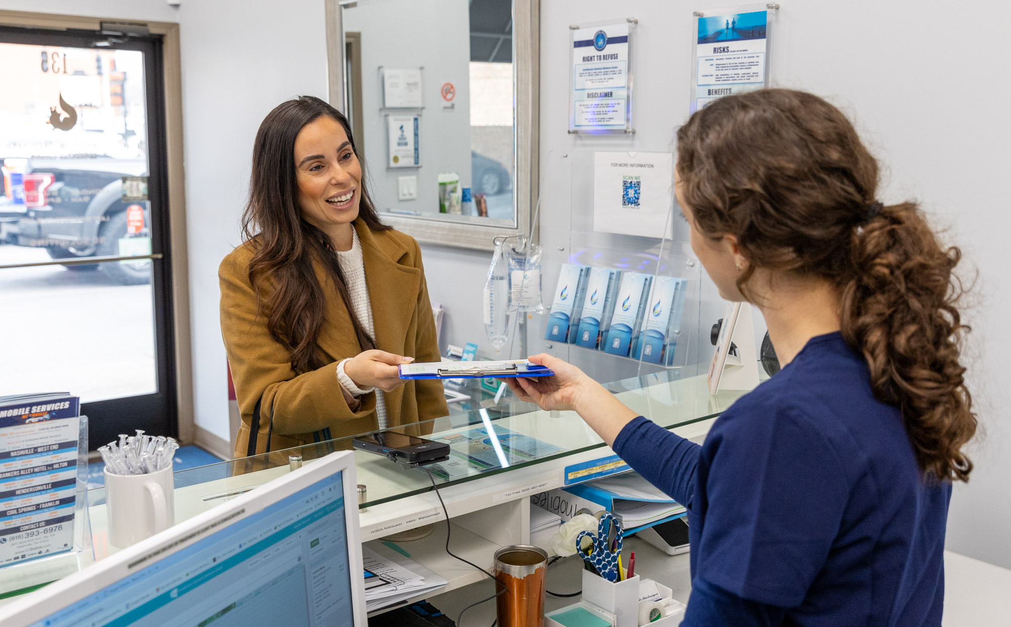 A medical staff member at the front desk welcomes a female patient in and has her fill out paperwork to receive an immunity boost in Nashville