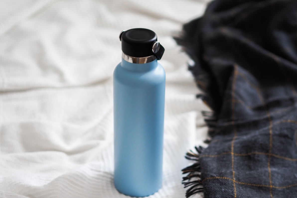 A blue water bottle with a black twist-off lid sits by a blanket, it is used to recover from a hangover after bachelorette party activities in Nashville.