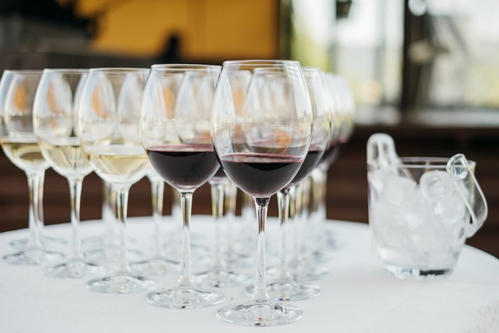 Long-stemmed wine glasses full of red and white wine are placed on a table next to a bucket of ice, in a triangular formation. The wine may make individuals seek hangover headache cures in Hendersonville. 